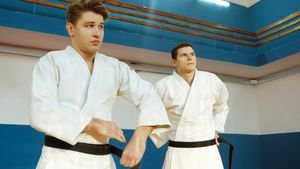 Two martial artists in white uniforms and black belts practicing indoors.